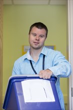 Caucasian man with Down Syndrome carrying bin in office