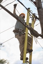 Caucasian cable installer working on ladder