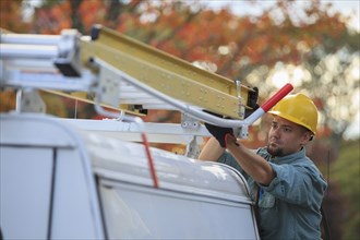 Caucasian worker loading ladder on truck