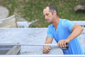 Deaf Caucasian roofer measuring skylight on roof