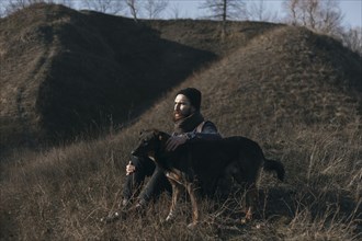 Caucasian man sitting on hill petting dog