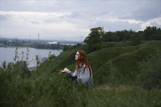 Pensive Caucasian woman sitting on hill near ocean