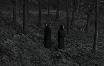People wearing black robes and white masks in forest