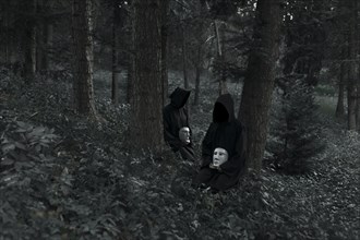 People wearing black robes and holding white masks sitting in forest