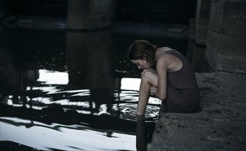 Pensive Caucasian woman sitting at edge of water