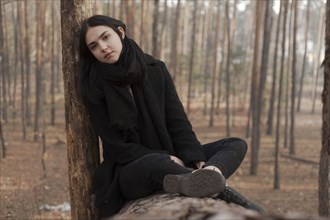 Serious Caucasian woman sitting on log in forest