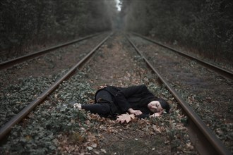 Caucasian woman laying on autumn leaves near train tracks in forest