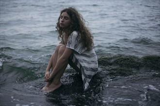Caucasian teenage girl sitting on rock in ocean