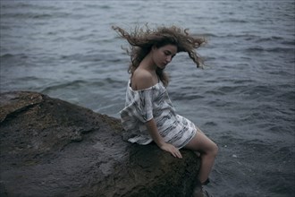 Wind blowing hair of Caucasian girl sitting at ocean