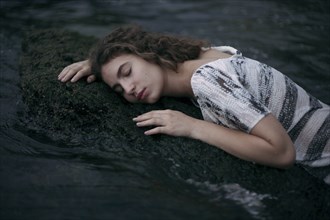 Caucasian girl laying face on a rock in ocean