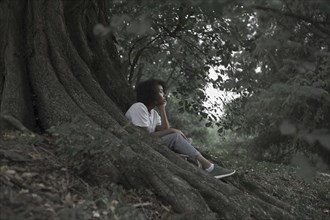 Pensive woman sitting on tree roots in forest