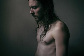 Pensive Caucasian man with long hair and bare chest