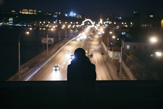 Silhouette of person watching traffic from overpass at night