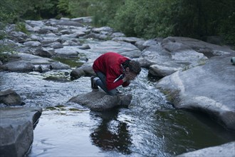Caucasian man kneeling on rock in river splashing water on face