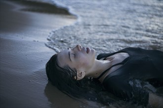 Caucasian woman laying on beach in waves