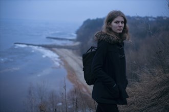 Caucasian woman wearing coat on cliff near ocean