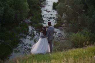 Caucasian bride and groom standing on hill admiring river