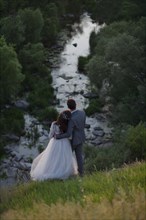 Caucasian bride and groom standing on hill admiring river