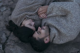 Caucasian couple laying on rock wrapped in blanket