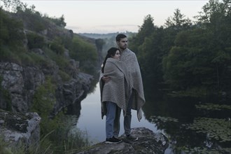 Caucasian couple wrapped in blanket standing on rock near river