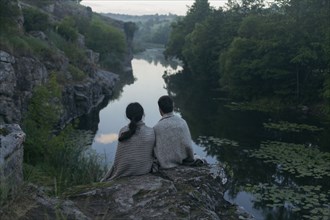 Caucasian couple wrapped in blanket sitting on rock admiring river