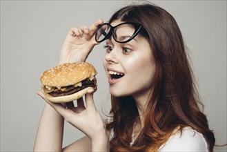Caucasian woman lifting eyeglasses looking at cheeseburger