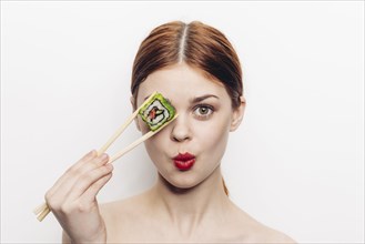 Caucasian woman holding sushi with chopsticks over eye