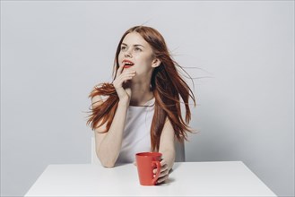 Pensive Caucasian woman sitting at windy table holding red cup