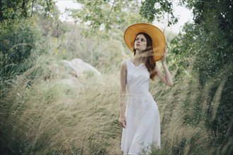 Caucasian woman wearing hat walking in tall grass