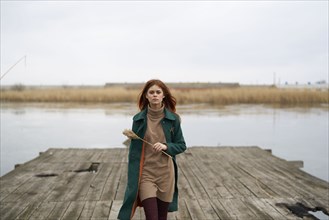 Serious Caucasian woman walking on dock holding stalk of grass