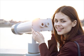 Smiling Caucasian woman using binoculars at waterfront