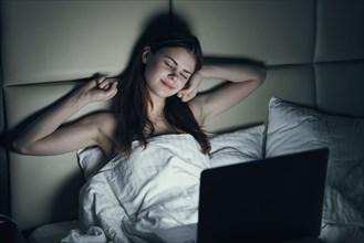 Fatigued Caucasian woman using laptop in bed