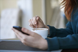 Caucasian woman texting on cell phone and stirring coffee