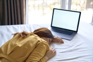 Fatigued Caucasian woman sleeping on bed near laptop