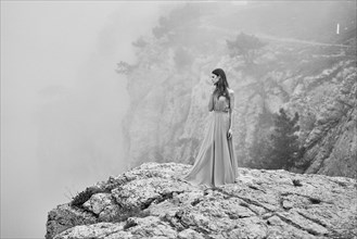 Woman wearing dress standing on rock in fog