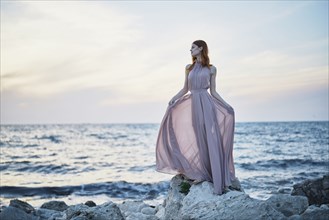 Caucasian woman wearing dress on rocks near ocean