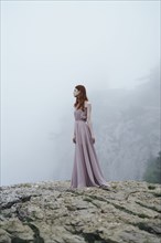 Caucasian woman wearing dress on rock in fog