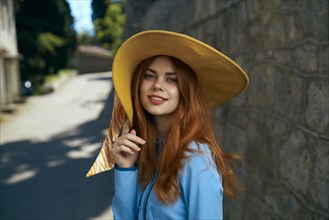 Smiling Caucasian woman wearing hat near stone wall