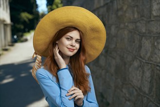 Smiling Caucasian woman wearing hat near stone wall