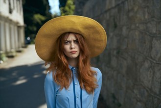 Frustrated Caucasian woman wearing hat near stone wall