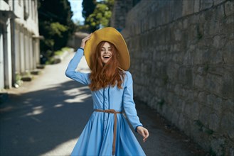 Laughing Caucasian woman wearing hat near stone wall