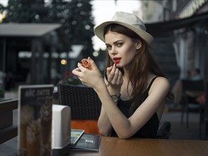 Caucasian woman at sidewalk cafe applying lipstick