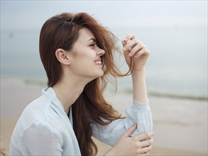 Smiling woman holding hair sitting on beach