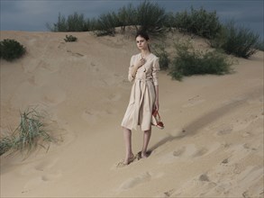 Caucasian woman wearing dress on beach carrying shoes