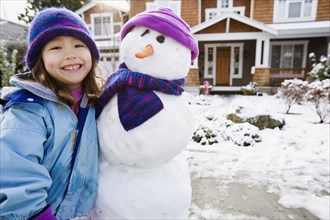 Portrait of girl with snowman in front yard