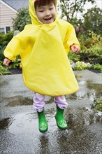 Young boy jumping in rain with rubber boots and raincoat on