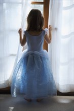 Rear view of girl dressed as princess and looking out window