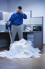 Businessman overlooking mountain of paper and holding rake