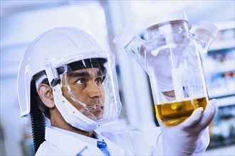 Indian male scientist wearing respirator and looking at beaker