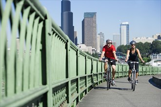 Couple riding bicycles on urban bridge